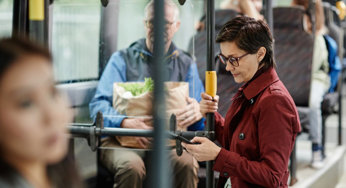 Eine Frau mittleren Alters steht in einem gefuellten Linienbus und schaut auf ihr Smartphone